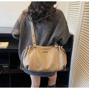 Back view of model wearing a beige lychee leather tote bag with drawstring detail