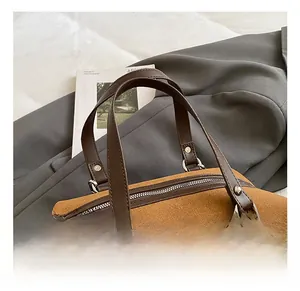 Detail shot of brown suede handbag featuring dark leather handles and silver metal rivets