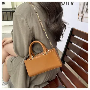 Brown faux leather crossbody bag with gold chain strap shown in an outdoor lifestyle setting