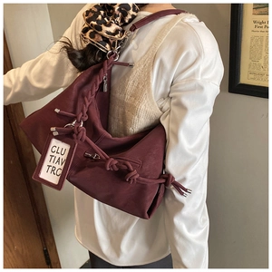 Detail of red-brown leather tote bag featuring knotted shoulder strap and branded tag