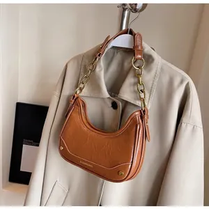 Close-up of caramel leather crescent bag featuring a gold chain strap and metal logo