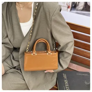 Detail of caramel faux leather crossbody bag with elegant gold chain strap on wooden bench