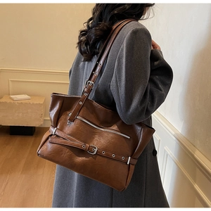 Detail view of large brown textured leather tote bag on model shoulder with silver zippers