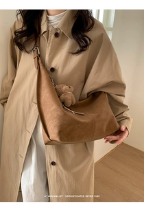 Detail of a brown Hobo crossbody bag with a plush bear charm on a khaki trench coat