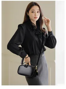 Close-up of black litchi leather handbag with gold double zippers and slender shoulder strap