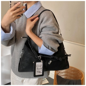 Detail of minimalist black dumpling bag with braided rope strap and decorative card accessory