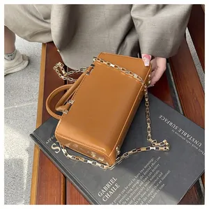 Detail of tan faux leather box bag with gold square link chain on a black book