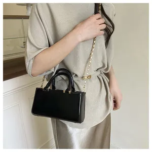 Close-up of black glossy tote bag featuring golden metal chain and dual handles