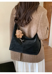 Detail of minimalist black suede shoulder bag with a cute brown plush bear charm