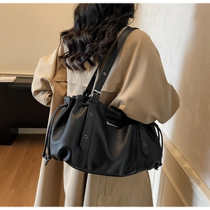 Detail of black pebbled leather tote bag featuring drawstring side and metal rivets on strap