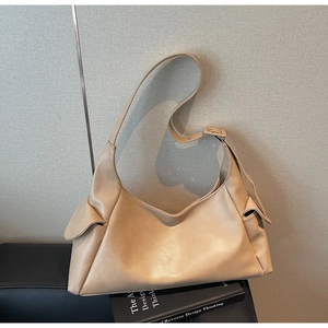 Detail view of large beige faux leather tote bag with side flap pockets on a black bench