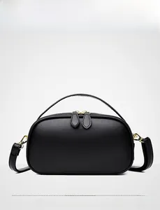 Front view of a black genuine leather round handbag featuring double gold zippers and top handle