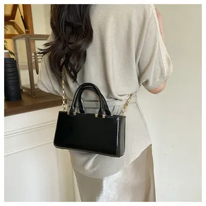 Detail view of glossy black leather tote with elegant gold chain strap and smooth finish