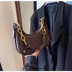 Detail of a dark brown crescent bag with glossy oil wax finish and gold chain strap