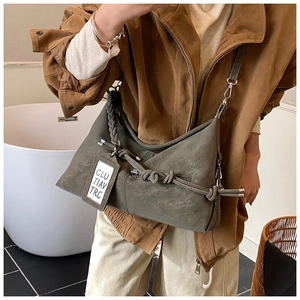 Detail of olive green crossbody bag with textured woven knot and artistic tag design