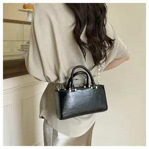 Model wearing a glossy black rectangular tote bag with elegant gold chain shoulder strap