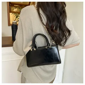 Detail view of a black glossy tote bag with golden chain strap on a model shoulder