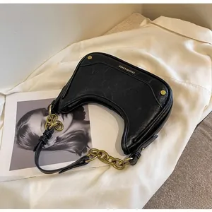 Detail of black crescent shoulder bag featuring gold chain and vintage crackle texture leather