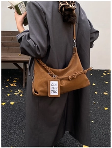 Brown moon-shaped crossbody bag with woven handle details shown in an autumn street setting