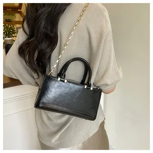 Detail of black glossy handbag with gold chain strap and bottom studs shown on model