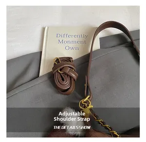 Detail of adjustable brown leather shoulder strap with golden buckle and chain on plaid bag