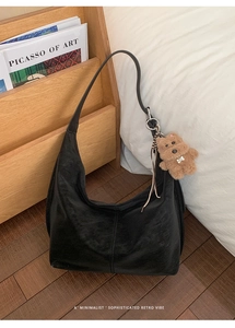 Detail of a black large Hobo tote bag with a plush bear charm on a wooden shelf