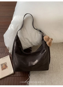 Close-up of vintage brown oversized hobo bag with teddy bear charm on white bedding