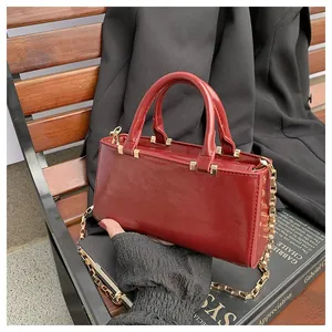 Detail of burgundy glossy leather tote bag with gold chain strap on a black suit