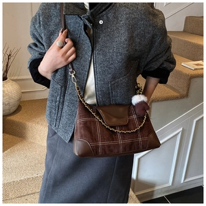 Detail of dark brown suede crossbody bag with grid stitching and gold chain strap