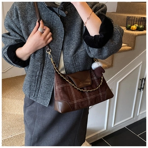 Detailed view of dark brown checkered crossbody bag with chic fur pom-pom and chain strap