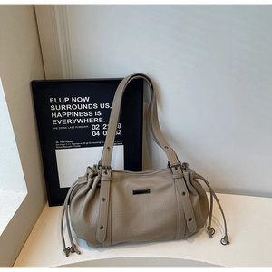 Detail of taupe litchi grain leather tote bag with drawstring sides and metal logo plate