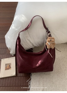 Detail of burgundy leather hobo bag featuring a cute plush bear charm in home setting