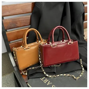 Close-up of burgundy and brown leather mini tote bags with gold chains on a wooden bench