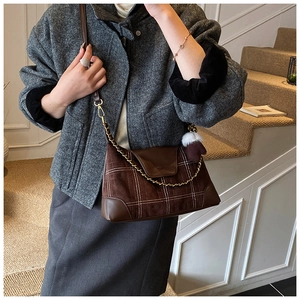 Detail of a brown suede crossbody bag featuring white grid stitching and plush ball charm