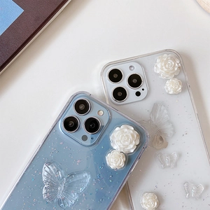 Détail de coque iPhone pailletée avec roses en résine 3D et papillons sur fond bleu et clair