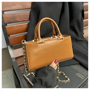 Detailed view of a brown faux leather tote bag with gold chain strap on a wooden bench