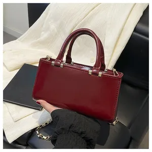 Detailed view of glossy burgundy leather tote bag with gold chain strap on vintage background