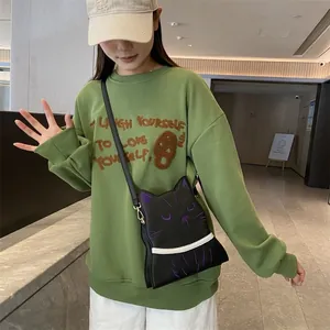 Détail du sac bandoulière chat noir avec broderie violette sur un sweat vert