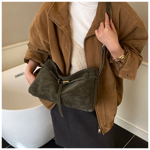 Detail of dark green suede tote bag with gold buckle on shoulder of model in autumn coat