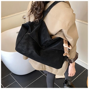 Close-up of black matte tote bag with wide strap and beige teddy bear charm