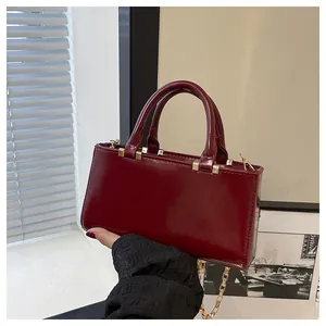 Detail of burgundy glossy tote with dual handles and gold chain strap