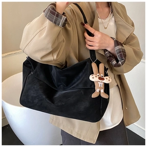 Detail of a large black faux leather tote bag with a beige bunny charm for daily commuting