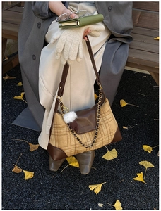 Close-up of retro plaid shoulder bag with metal chain and fur ball charm on autumn leaves