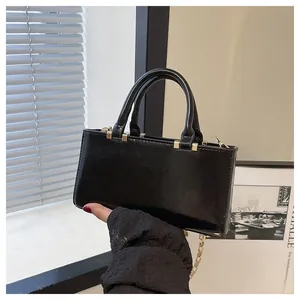 Detail of a black glossy handbag with golden chain strap and sturdy top handles