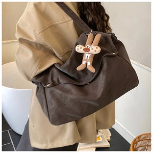 Detail of dark brown matte tote bag featuring a cute plush bunny charm and wide shoulder strap