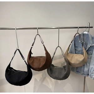 Quattro borse a mezzaluna in camoscio colorato appese con una giacca di jeans su stand