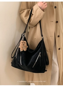 Detail of black textured hobo bag with zip pockets and bear charm on model shoulder