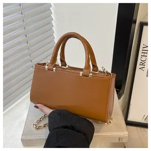Detail of a brown leather tote bag with round handles and a gold chain strap