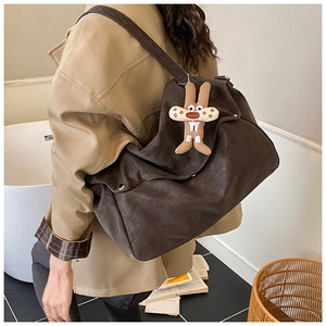Macro detail of brown leather tote bag strap with wide stitching and rabbit charm