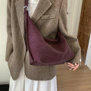 Large burgundy half-moon crossbody bag in textured leather worn by a model in a casual outfit